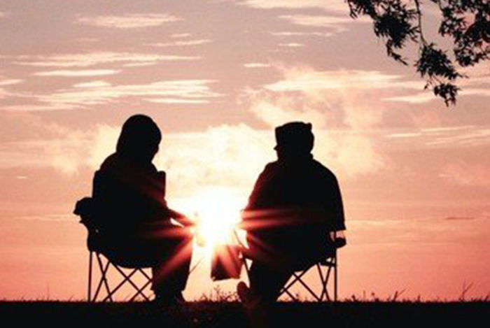 Silhouetten von zwei Personen, die bei Sonnenuntergang sitzen.