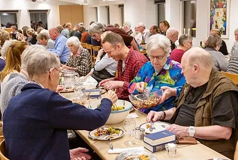 Viele Menschen essen an Tischen in einem vollen Raum.