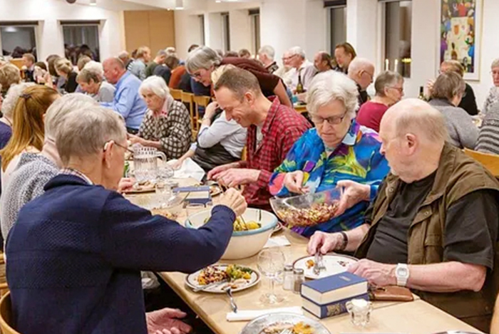 Viele Menschen essen an Tischen in einem vollen Raum.