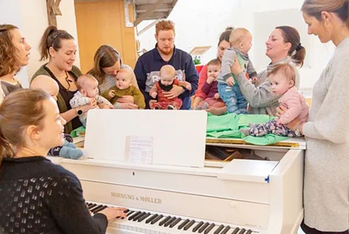 Erwachsene und Babys bei einer Aktivität mit einem weißen Klavier.