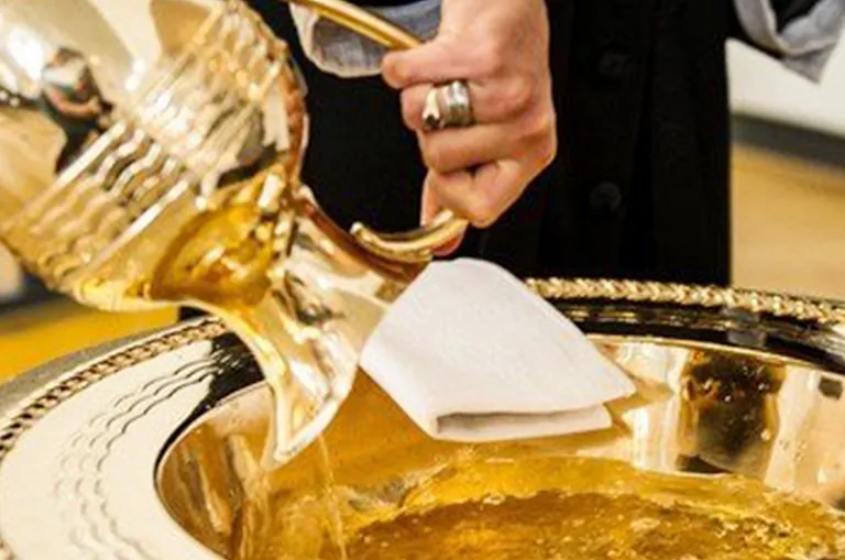 Eine goldene Kanne gießt Flüssigkeit in eine Taufschale.
