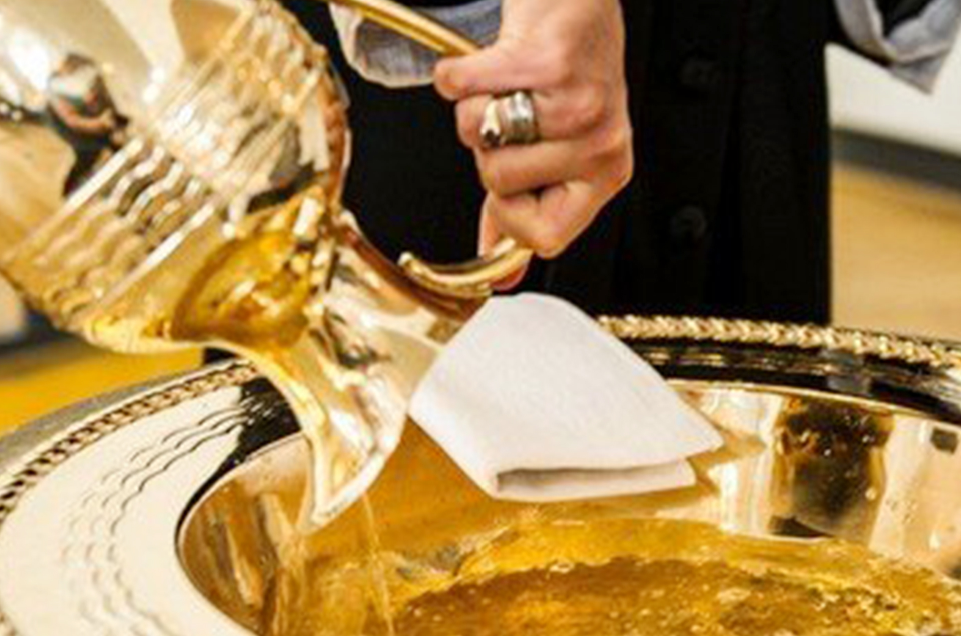 Eine goldene Kanne gießt Flüssigkeit in eine Taufschale.
